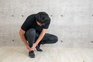 男性が足首を抑えてしゃがんでいる